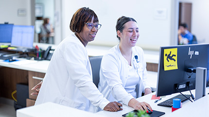 Nurse instructing grad student on computer.